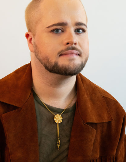 Model wearing wavy pendant bolo tie, green mesh shirt and tan jacket
