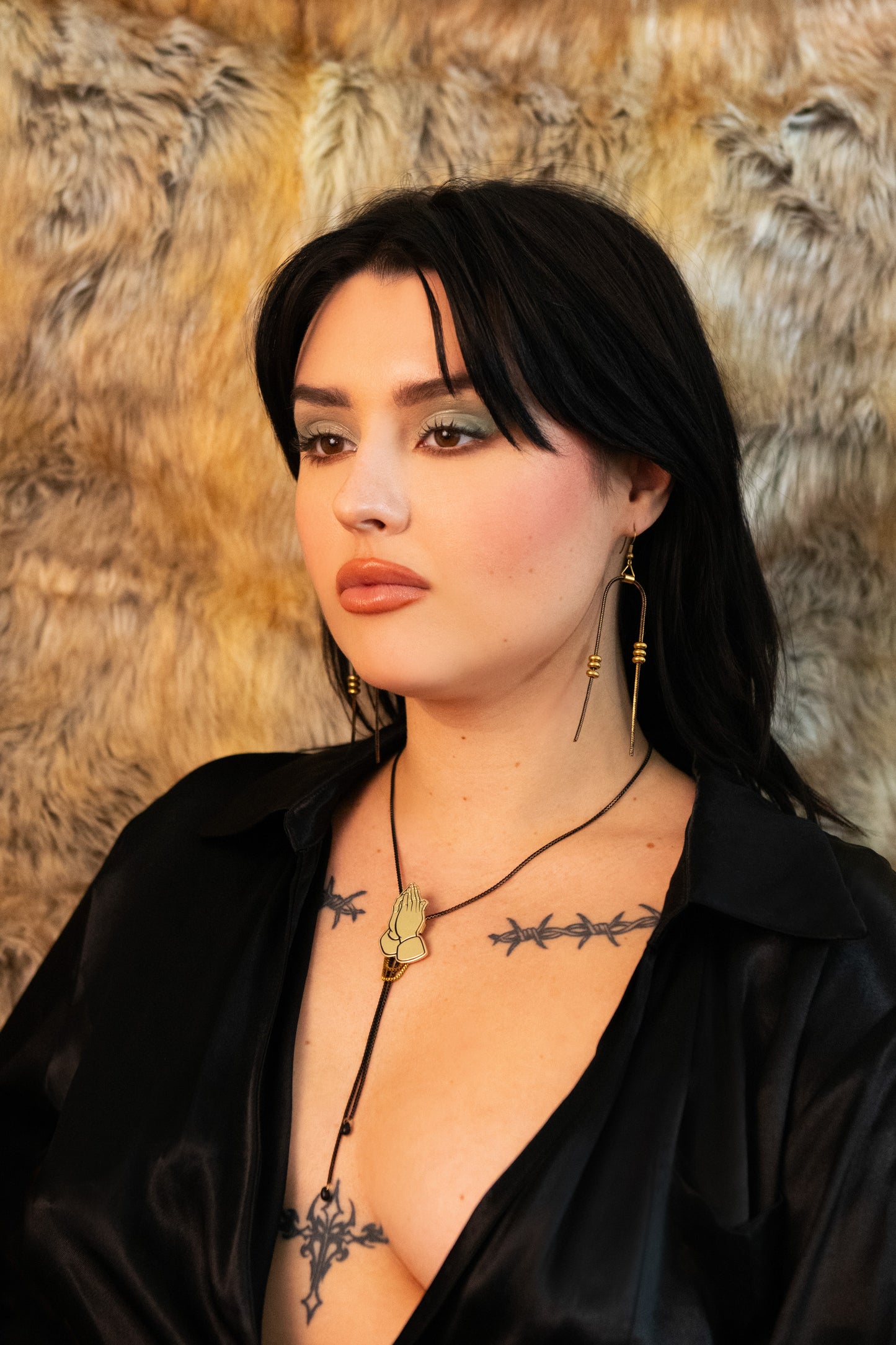Model wearing black and gold bead earrings, praying hands bolo tie and black V neck silk dress