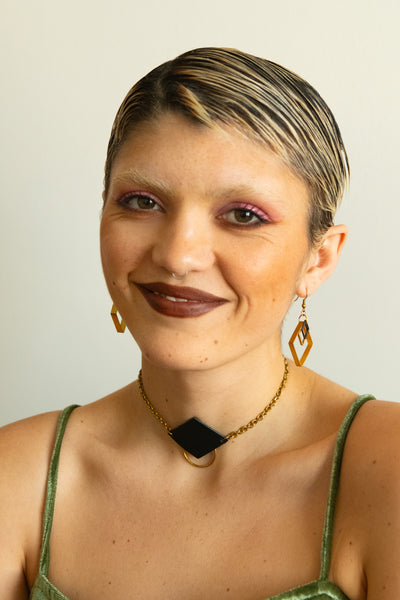 Model wearing geometric brass earrings, leather pendant choker and green velvet dress
