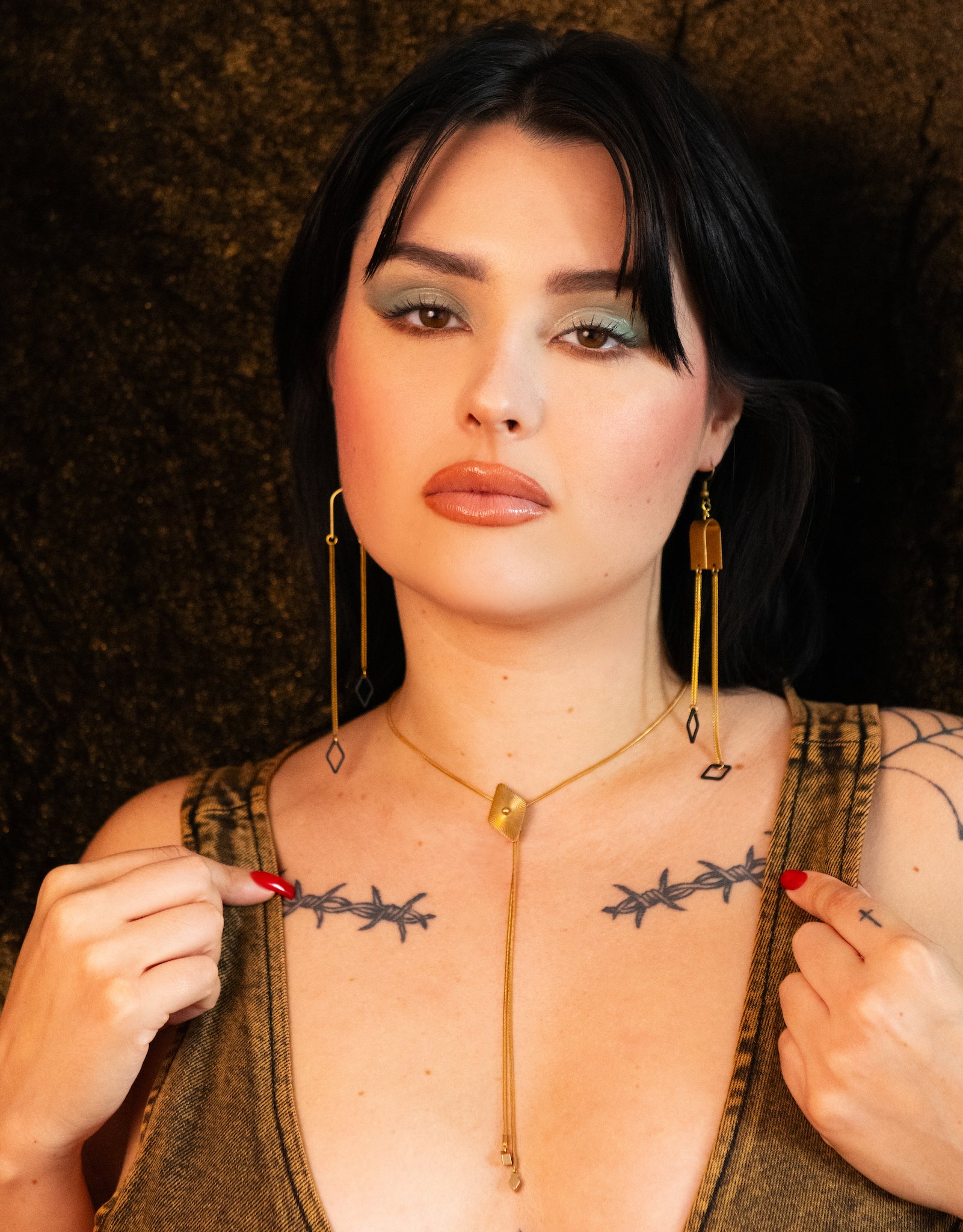 Model wearing brass diamond bolo tie, dangle earrings and brown denim tank top