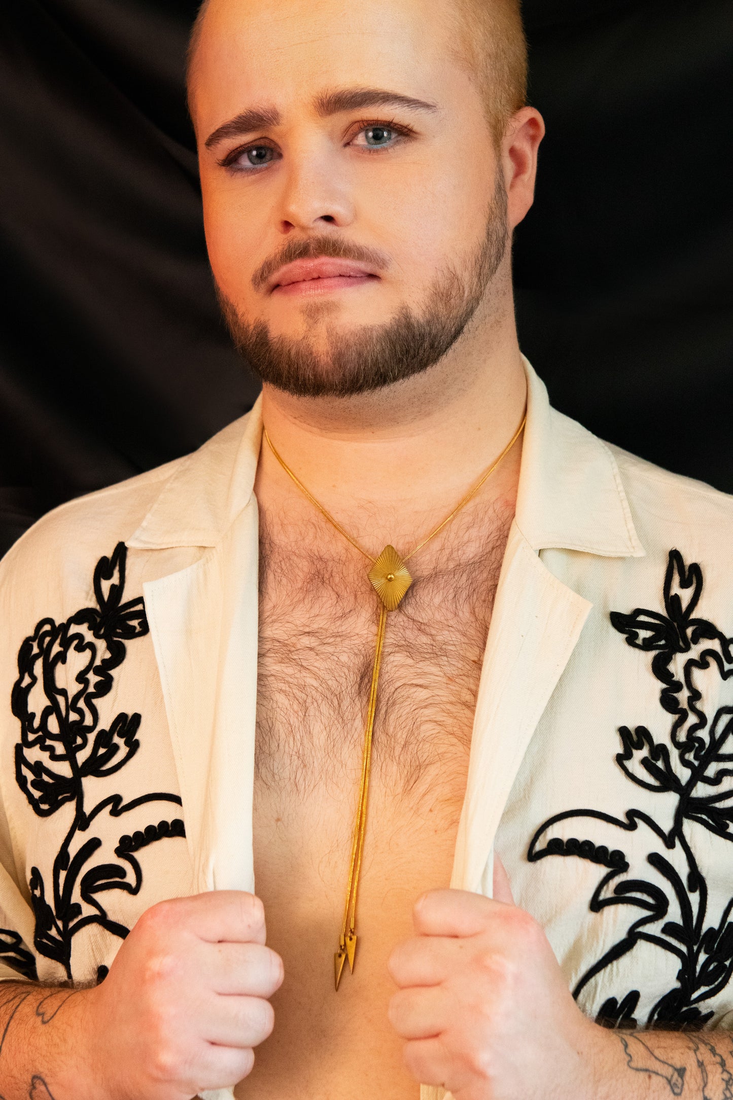 Model wearing diamond bolo tie and white blouse with black floral embroidery