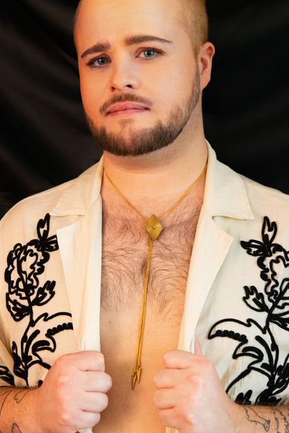 Model wearing diamond bolo tie and white blouse with black floral embroidery