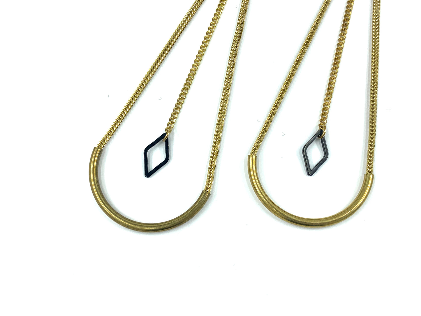 Close-up of earrings with curved tube bead and black diamond charm hanging from long chain