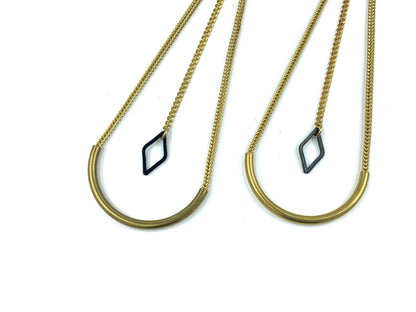 Close-up of earrings with curved tube bead and black diamond charm hanging from long chain