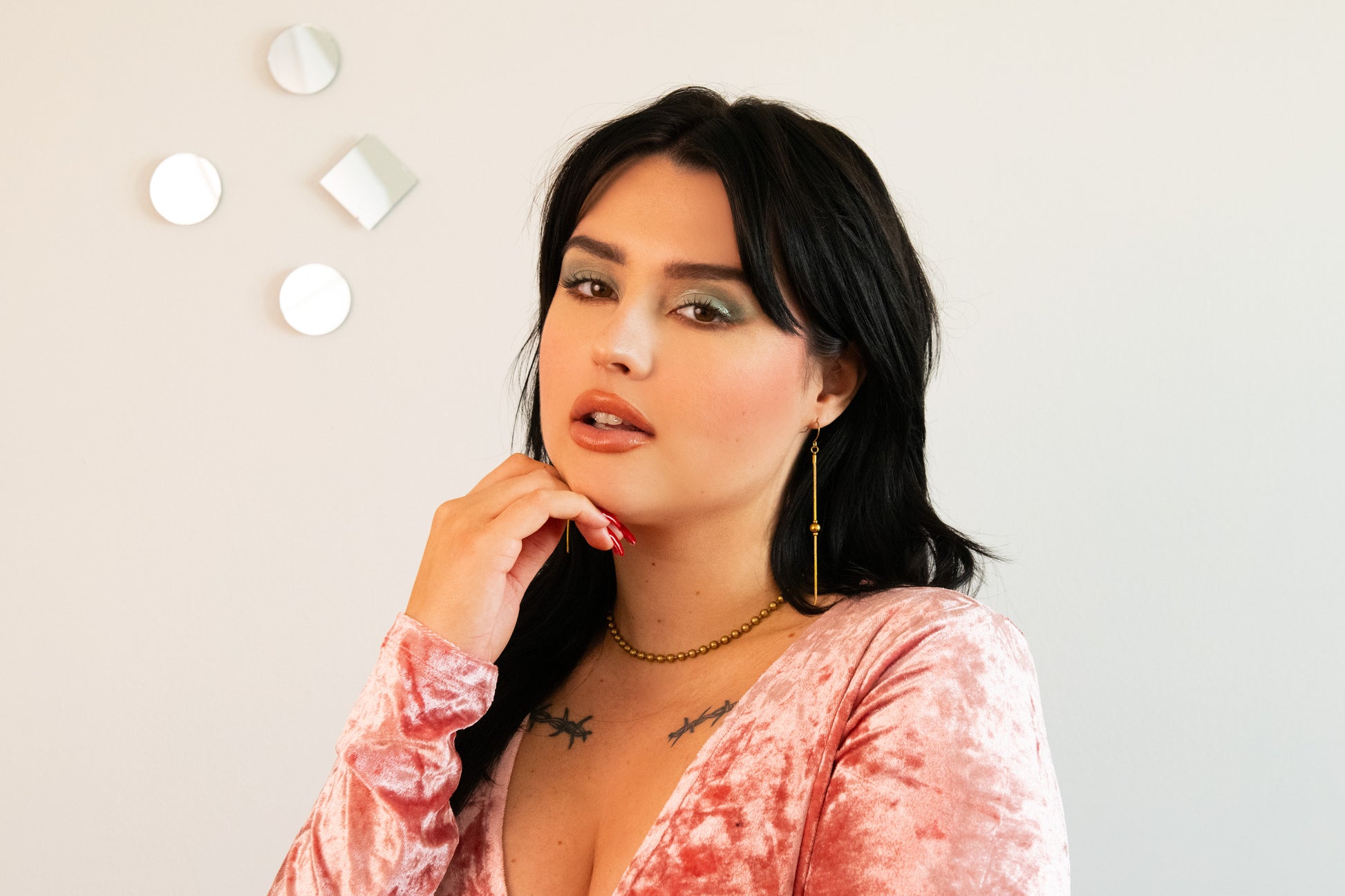 Model wearing gold drop earrings, ball chain choker and pink velvet top