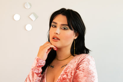 Model wearing gold drop earrings, ball chain choker and pink velvet top