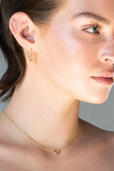 Close-up of model wearing gold captive barbell charm choker and matching earrings