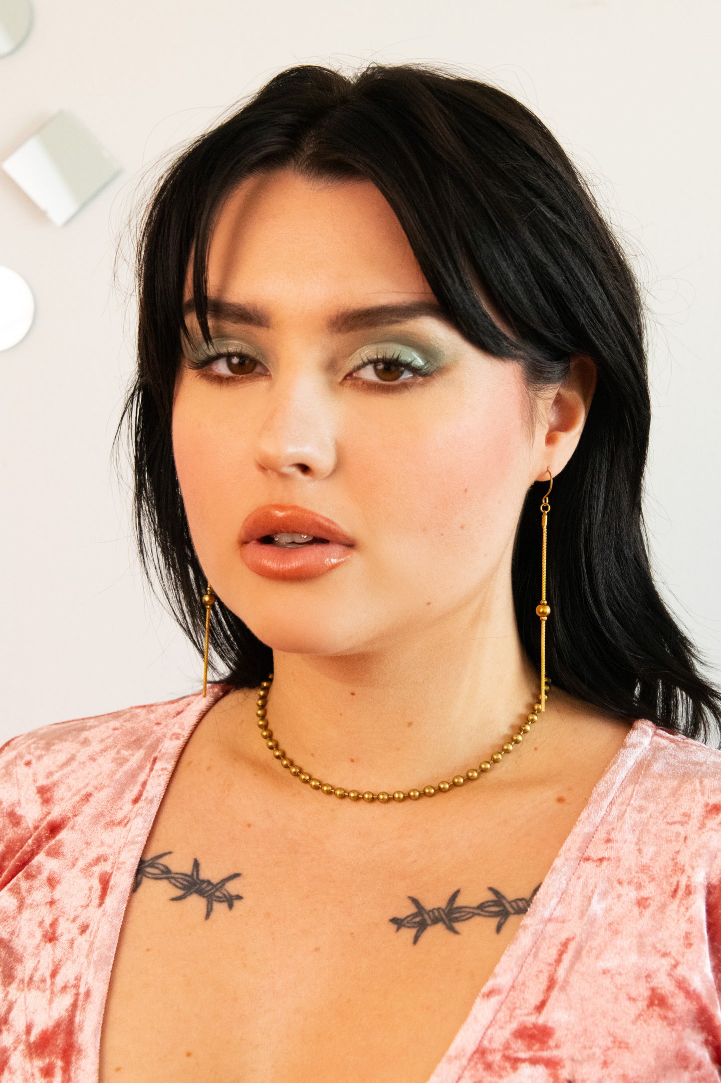 Model wearing shiny gold drop earrings, ball chain choker and pink velvet top