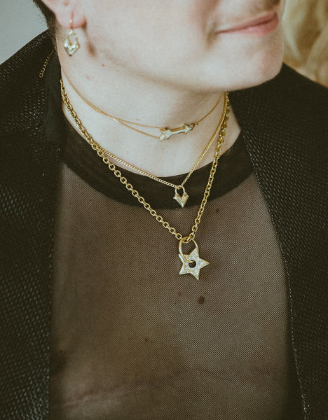 Close-up of model wearing black mesh shirt, gold arrow choker, heart charm choker and spur charm choker