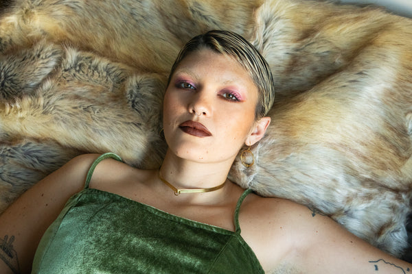 Model wearing gold collar and green velvet dress, laying on beige fur rug