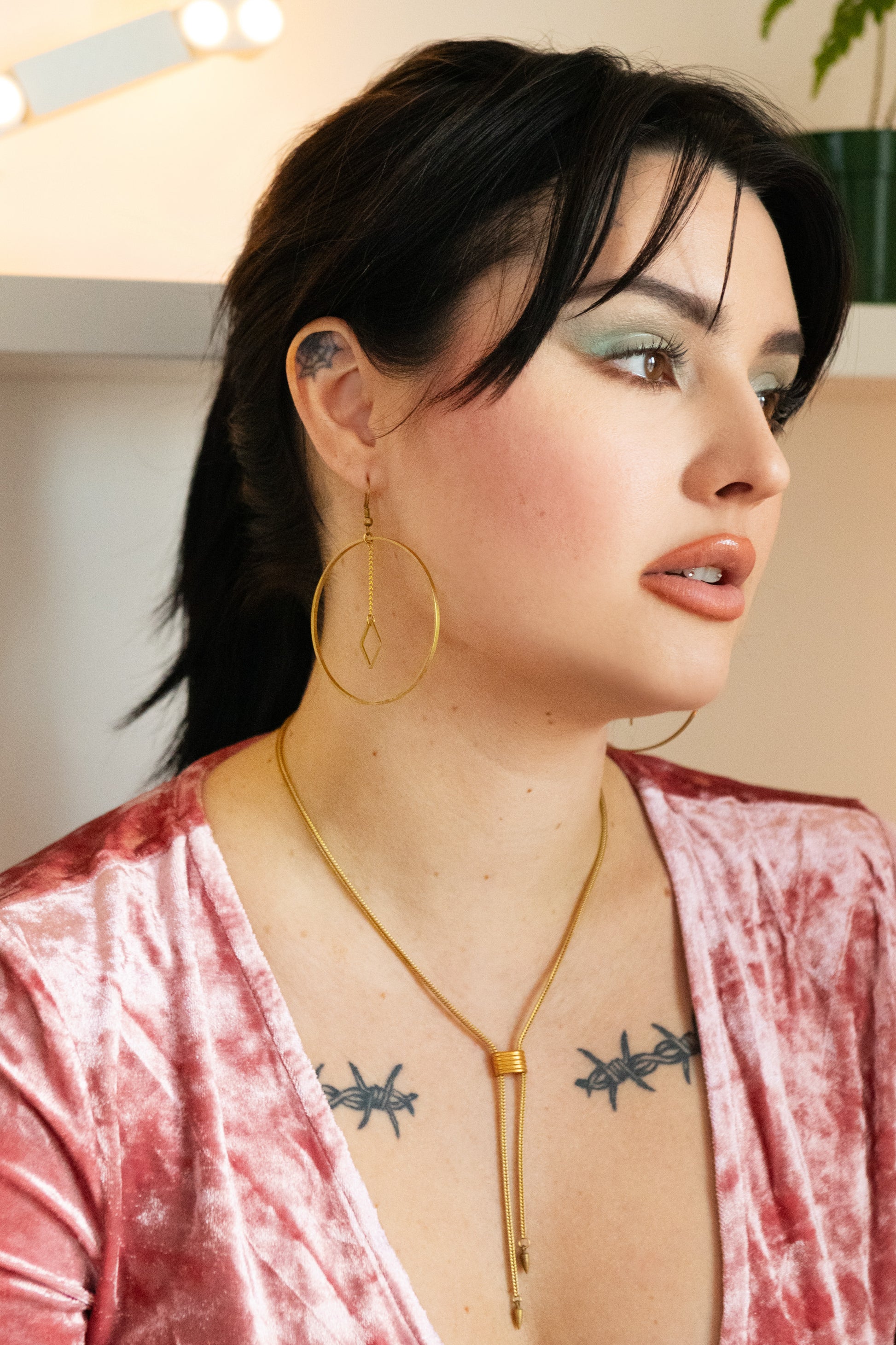 Model wearing oversized gold hoop earrings, gold choker necklace and pink velvet top