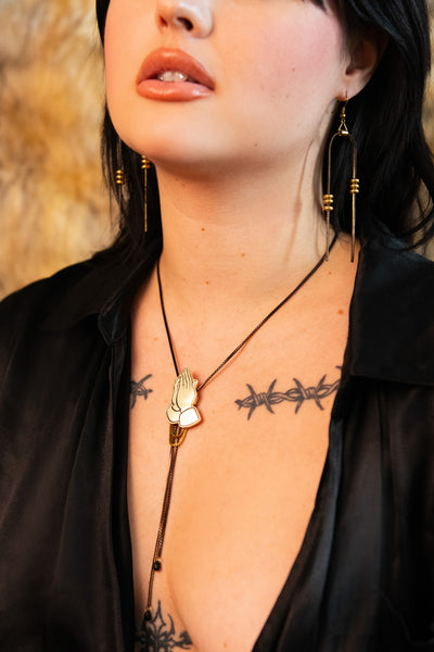 Close-up of model wearing praying hands bolo tie and black and gold chain earrings