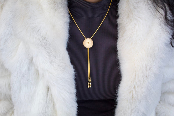 Close-up of model wearing small gold bolo tie necklace