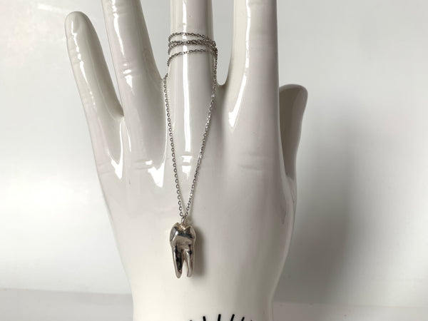 Close-up of sterling silver tooth pendant of choker with a delicate chian, ahnging from a ceramic hand in front of a white background