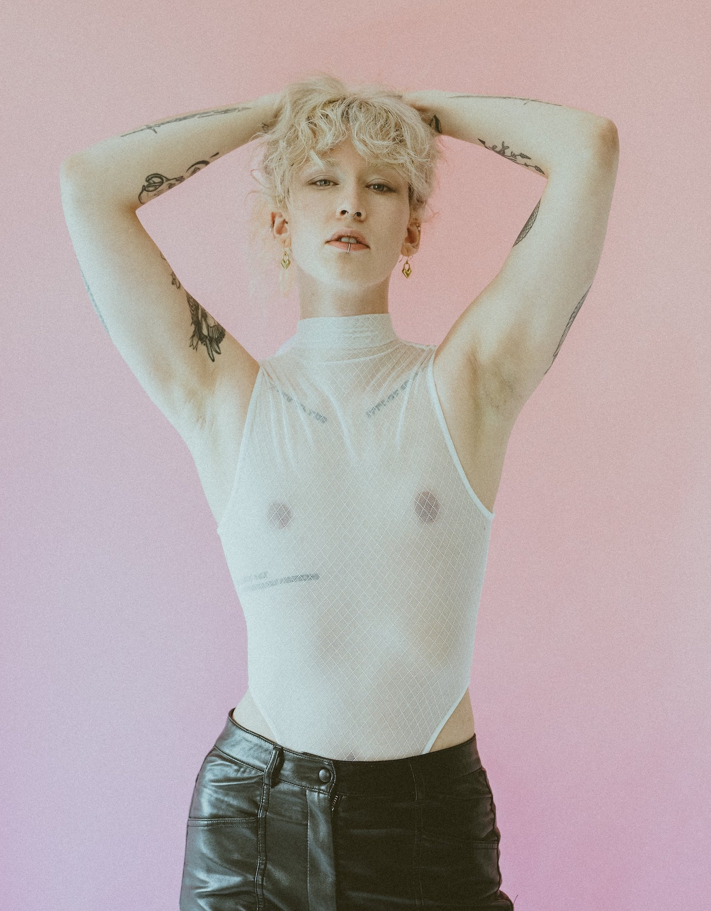 Model wearing gold heart earrings, white mesh bodysuit and black leather pants