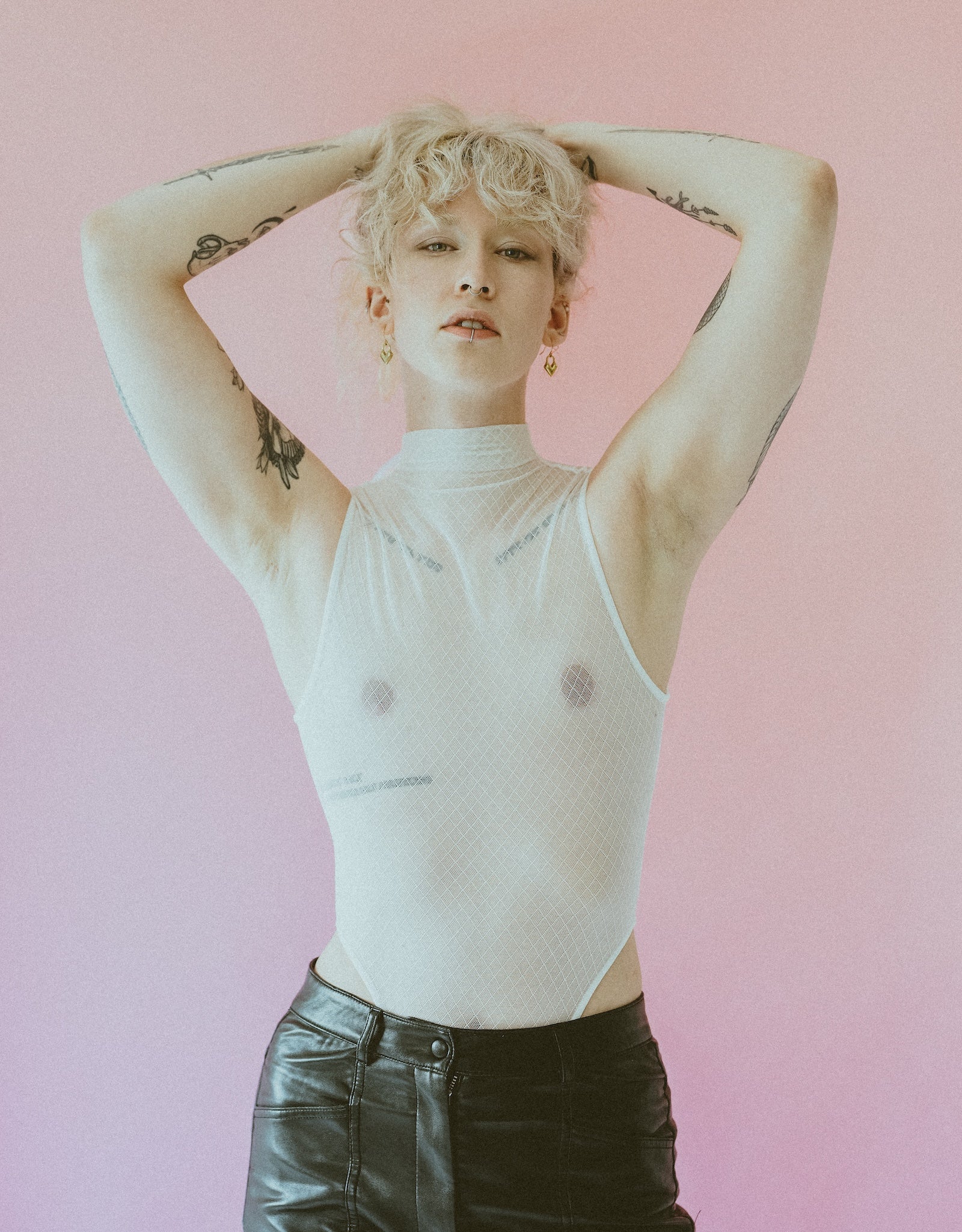 Model wearing gold heart earrings, white mesh bodysuit and black leather pants