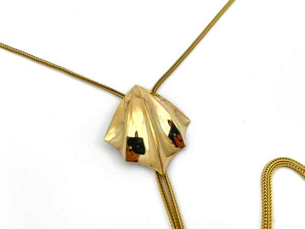Close-up of gold fin pendant of bolo tie on a white background