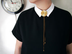 Model wearing gold and black bolo tie necklace