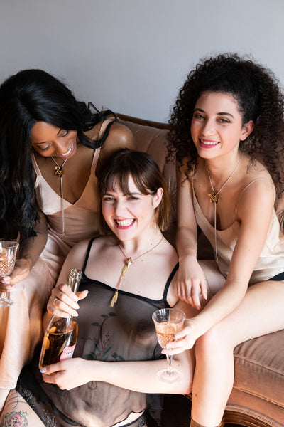 Models wearing flower bolo ti necklace and drinking champagne