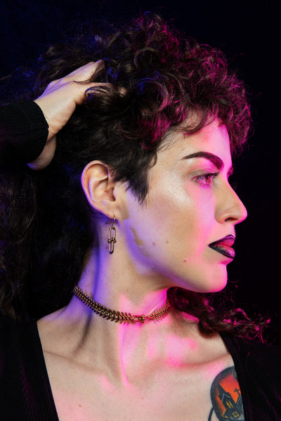 Side view of model wearing fishbone choker necklace, hardware earrings, holding up her hair