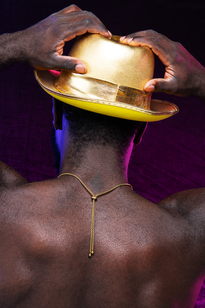 Model's back, wearing gold bolo tie necklace and gold cowboy hat