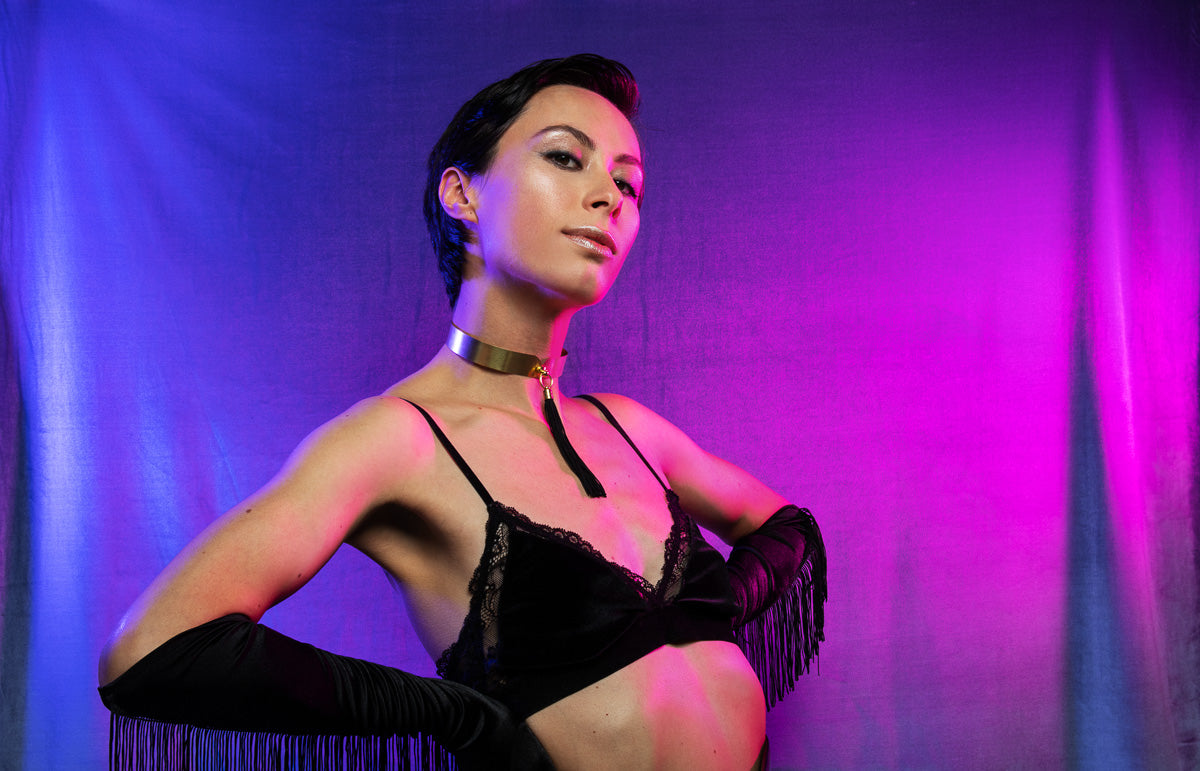 Model wearing gold choker with tassel, black velvet bralette and black tassel gloves